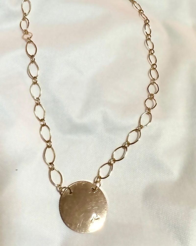 Round gold disc pendant on an open-link gold chain, against a white background
