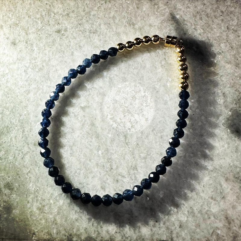 Bracelet of faceted deep-blue sapphire beads and a row of small gold beads, on grey stone