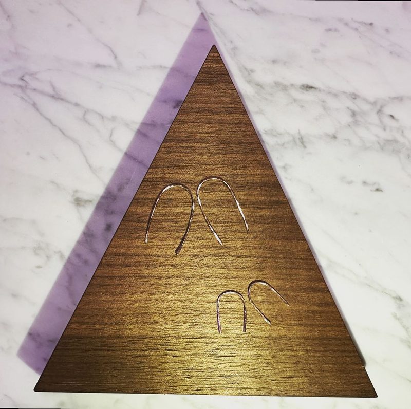 Two pairs of thin gold arch earrings, one larger and one smaller, on a triangular walnut display