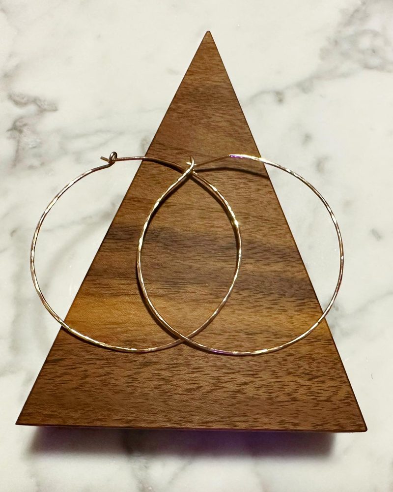 Pair of large, thin gold hoop earrings hanging over a triangular walnut display