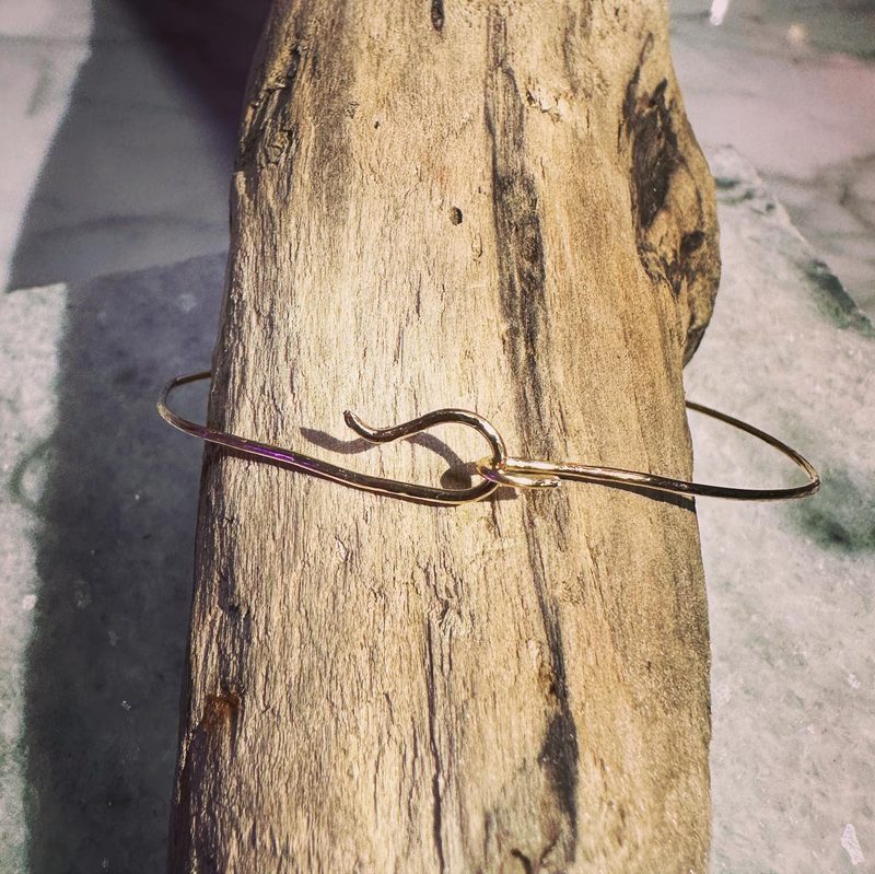 Hammered gold wire bracelet with a looped hook closure, wrapped around a piece of driftwood